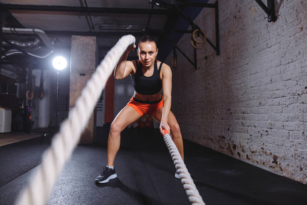 Young woman working out with battle ropes in cross fit gym - Fotoğraf, Görsel