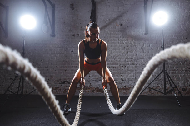 Young woman working out with battle ropes in cross fit gym - Photo, image