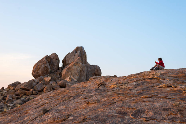 Donna seduta sulle rocce e guardando ampia vista sul pittoresco deserto Namib al crepuscolo. Viaggiare nel Namib Naukluft National Park, Namibia, Africa
.  - Foto, immagini
