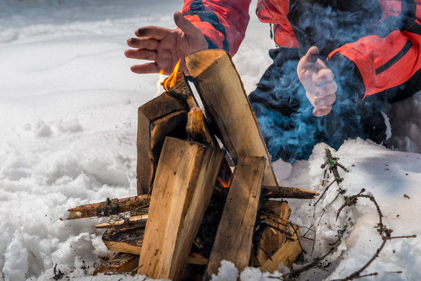 el turista construye un fuego en el bosque de invierno y calienta su han
 - Foto, Imagen
