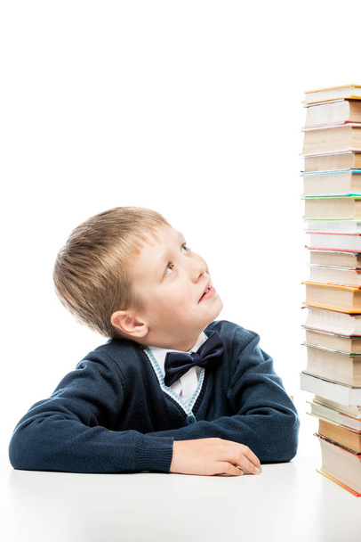 школьник смотрит на стопку книг на столе
 - Фото, изображение