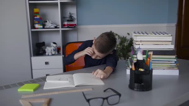 A boy is a schoolboy waking up at a table at which he did his homework. Tired child from homework. Books and notebooks on the table - Imágenes, Vídeo
