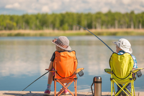 children with fishing rods sit on a wooden pier and fish at the  - Фото, изображение