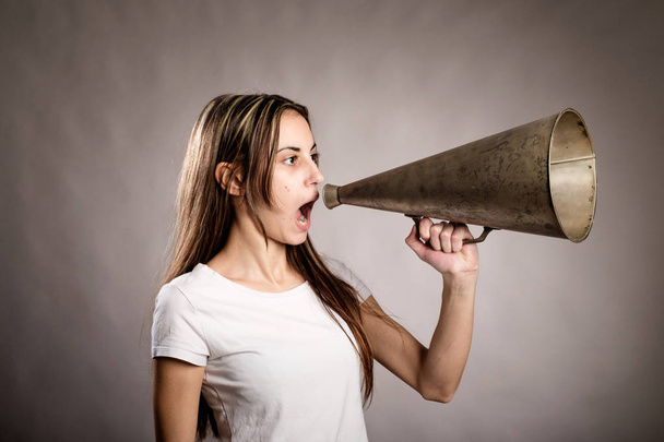 Молодая женщина кричит со старым мегафоном на сером фоне
 - Фото, изображение