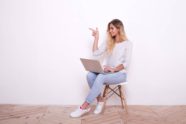 junge Frau sitzt auf dem Stuhl und arbeitet am Laptop. und zeigt seine Hand zur Seite - Foto, Bild