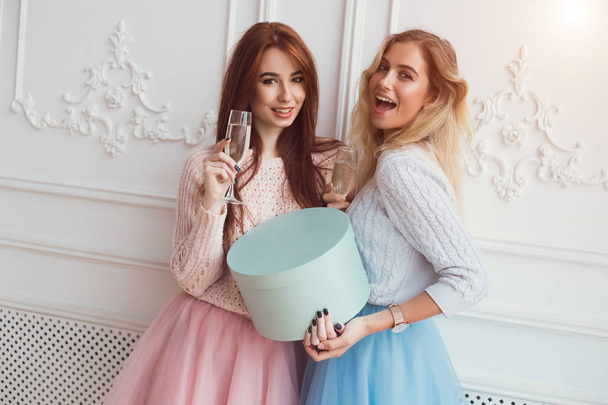 Dos chicas sostienen una caja de regalos. Están bebiendo champán y divirtiéndose. Celebración de la fiesta. Dar un regalo
. - Foto, Imagen