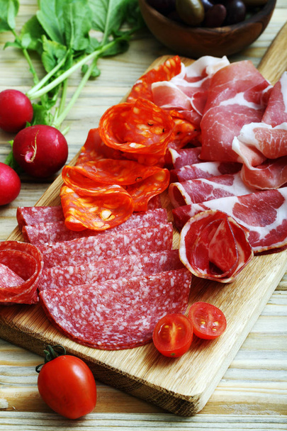 Gourmet set with prosciutto, pepperoni, salami slices served on wooden chopping board with cherry tomatoes, olives and radishes - Foto, Bild