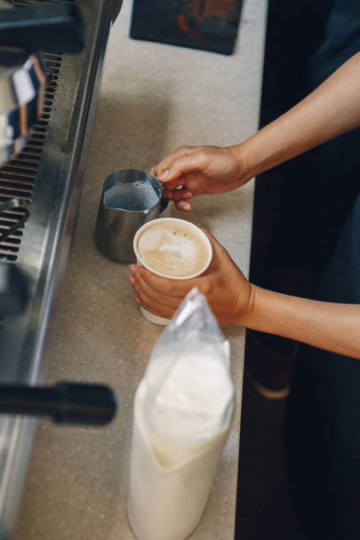 Nahaufnahme Makroaufnahme kaukasischer Barista-Hände bei der Herstellung von Cappuccino. Kellner oder Kleinunternehmer gießt heiße Milch in Kaffeepapierbecher. - Foto, Bild