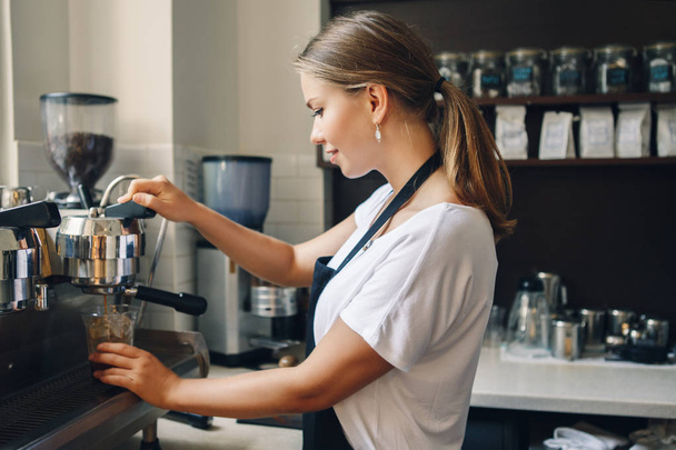 Portrait of happy beautiful young Caucasian smiling woman barista holding plastic cup with ice. Server making cold drink in coffee shop. Small business owner and person at work concept. - Фото, изображение