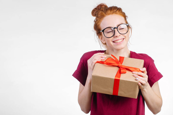 Happy redhead woman in glasses holding gift box on white background - Valokuva, kuva