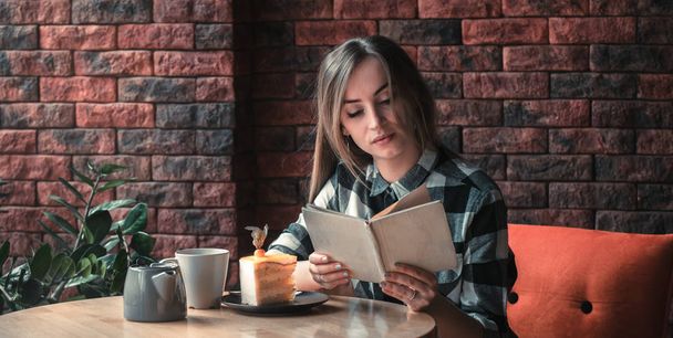Όμορφο κορίτσι διαβάζει ένα βιβλίο σε ένα καφέ - Φωτογραφία, εικόνα