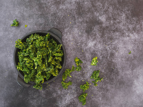 Kale chips with salt in a bowl on dark background. Top view, blank space - Valokuva, kuva