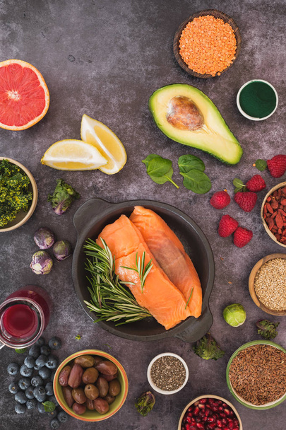 Healthy food ingredients on dark rustic table featuring fish, seeds, legumes, fruits and vegetables. Top view, blank space - Fotografie, Obrázek