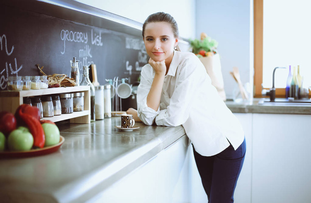 Portrait of young woman standing against kitchen background. - Fotografie, Obrázek