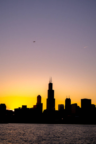 Chicago skyline beeld tijdens mooie oranje gele zon als het verlaagt onder het gebouw silhouetten en het water van lake Michigan in de voorgrond - Foto, afbeelding