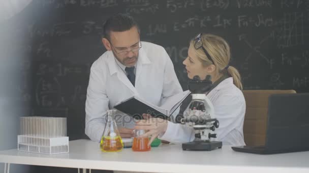 4K Scientists working in lab writing chemistry and maths formulas on blackboard - Filmati, video