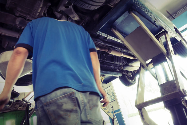 Autoservice, reparatie & onderhoud. Professionele auto monteur man aan het werk onder opgeheven auto in auto reparatieservice. - Foto, afbeelding