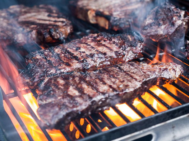 Close-up photograph of various cuts of beef including filet mignon and t-bone steak on a gas fire grill for a backyard barbeque. - Zdjęcie, obraz