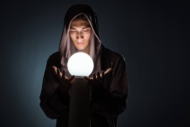 Young wizard with crystal ball in dark room - Foto, imagen
