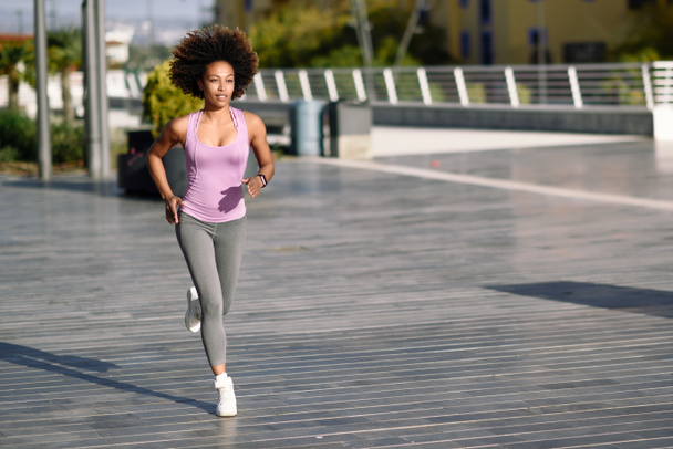 Black woman, afro hairstyle, running outdoors in urban road.  - Фото, зображення