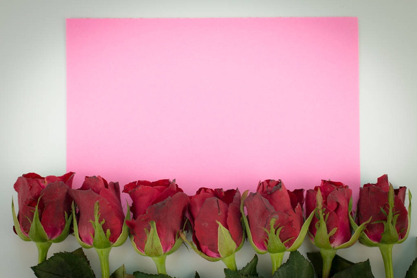 Κοντινό πλάνο της κόκκινα τριαντάφυλλα σε φόντο ξύλινη με κενό μήνυμα σημάδι για σας κείμενο ή μήνυμα. ροζ ευχετήρια κάρτα με ένα κόκκινα τριαντάφυλλα και χώρο για κείμενο χρησιμοποιώντας ως αγάπη, ημέρα του Αγίου Βαλεντίνου ημέρα έννοια. - Φωτογραφία, εικόνα