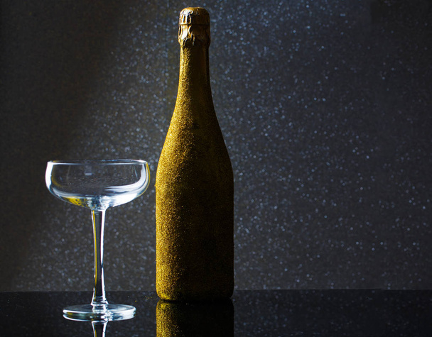 Photo of bottle of champagne in gold wrapper with empty wine glass - Foto, imagen