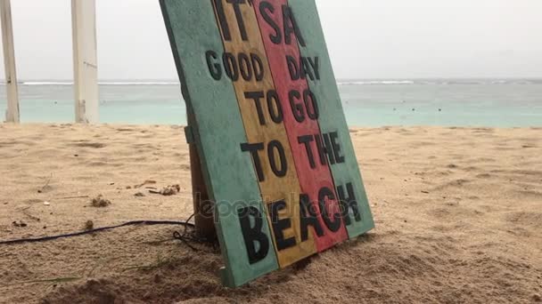 Tropisch strand in een regenachtige dag. Houten bord met tekst is een goede dag om naar het strand te gaan. Bali eiland. - Video