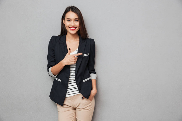 Uśmiechnięta kobieta azjatycki biznes z ręką w kieszeni, wskazując od - Zdjęcie, obraz