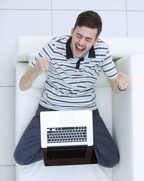 view from the top. jubilant young man with laptop sitting on the couch - Foto, Imagem