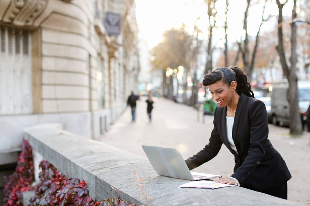 Half African businesswoman making video call with laptop outside - Foto, Bild