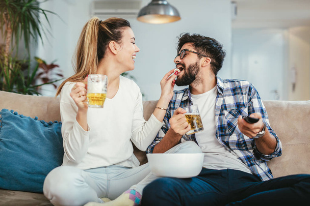 Пара смотреть телевизор в гостиной во время еды попкорн и пить пиво
 - Фото, изображение