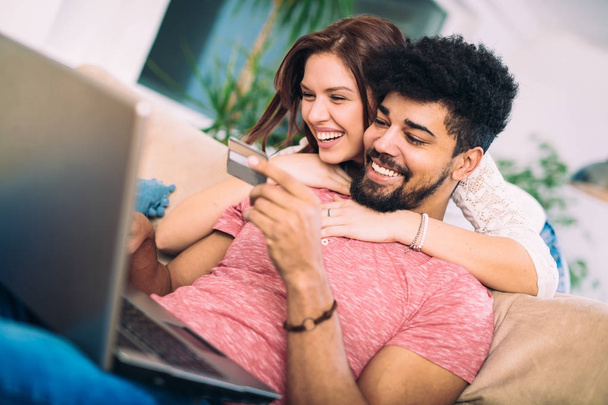 Szczęśliwa para międzyrasowy zakupy online w domu, przy użyciu karty kredytowej, śmiejąc się - Zdjęcie, obraz