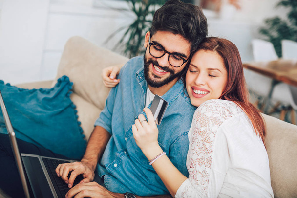 Мужчина использует ноутбук, а женщина держит кредитку. Молодая пара покупок онлайн с кредитной картой в доме
 - Фото, изображение