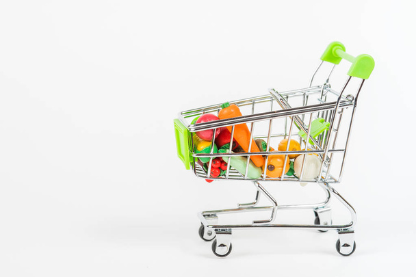 Játékos miniatűr bevásárlókocsi színes túlméretezett gyümölcsök és zöldségek választékával - Fotó, kép