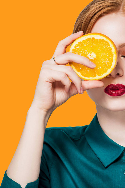 Beautiful redhead girl with professional makeup red lips with closed eyes in a green shirt with orange closes one eye lip kiss closeup orange background - Photo, image