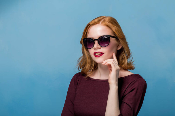 Close up shot of stylish young woman in sunglasses smiling against blue background. Beautiful female model with copy space. - Fotografie, Obrázek