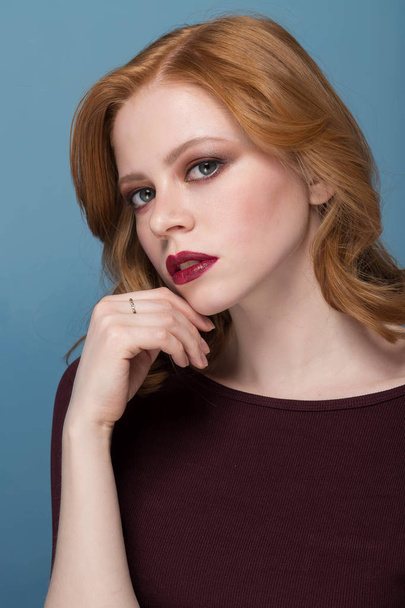 Mistrust and puzzled redhead woman, looking at camera. Studio shot. Redhead beautiful girl with bright makeup on a blue background. - Zdjęcie, obraz