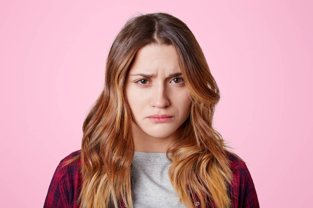 Attractive offended female with dissatisfied expression, curves lips, going to cry as being abused by close person, didn`t expect such bad attitude towards her, isolated over pink background - Фото, изображение