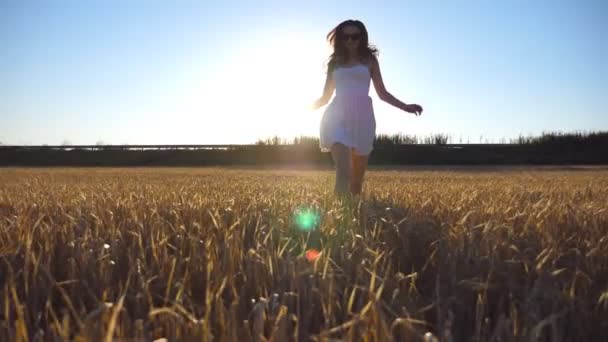 Joven chica hermosa corriendo a lo largo del campo de trigo con destello de sol en el fondo. Mujer caucásica corriendo a la cámara en el hermoso prado. Vista frontal cámara lenta Primer plano
 - Metraje, vídeo