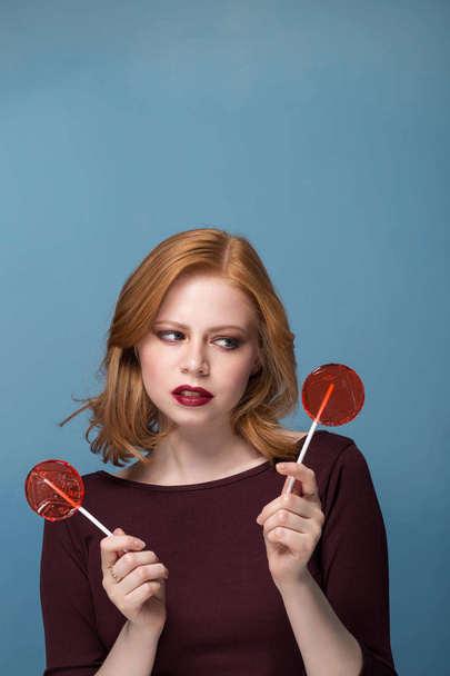 Portrait of a young woman in the two red lollipop on a blue background. The concept of choice, copys pace. - Foto, Imagem