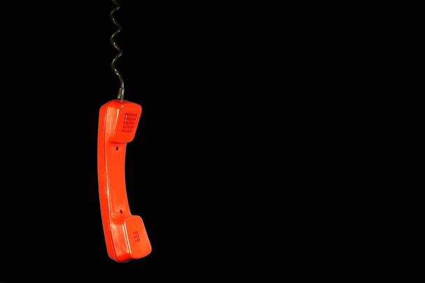 Качание в воздухе ярко-красного старого ротационного телефонного аппарата висящего изолированно на черном фоне иллюстрирует потерю связи или другую концепцию проблемы. Пространство для копирования текста
. - Фото, изображение