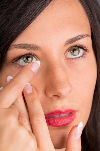 Молодая женщина кладет контактные линзы в глаз. - Фото, изображение
