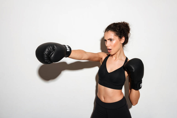 Serious curly brunette fitness woman trains in boxing gloves - 写真・画像