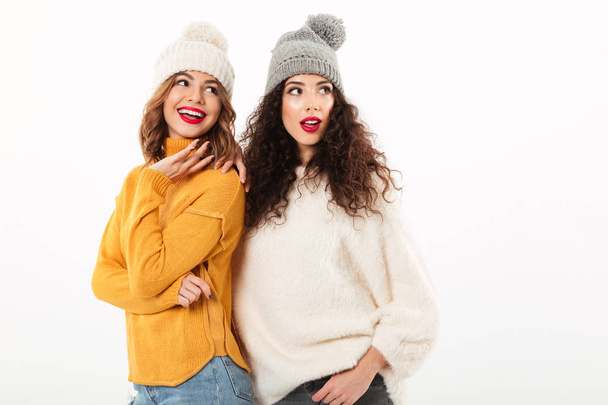 Two smiling girls in sweaters and hats standing together - Zdjęcie, obraz
