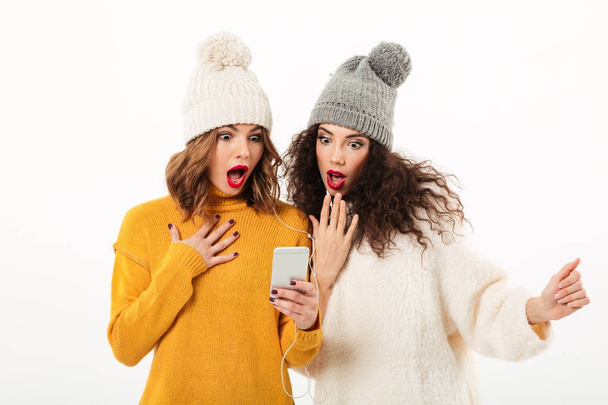 Two shocked girls in sweaters and hats standing together - Foto, Imagen