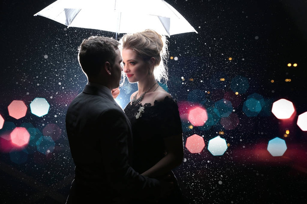 Beautiful couple man with woman  with  white umbrella in flash lights and rain drops - Foto, Imagen