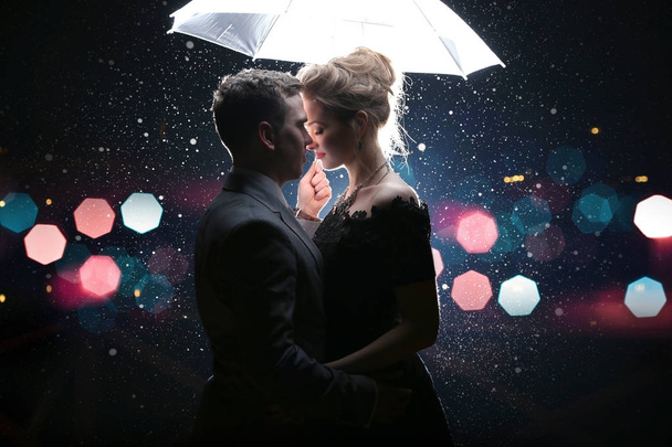Beautiful couple man with woman  with  white umbrella in flash lights and rain drops - 写真・画像