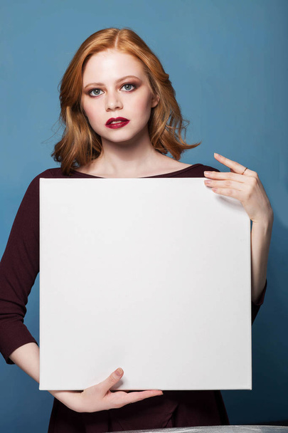Portrait of a young redhead woman holding a white blank banner. - Fotoğraf, Görsel