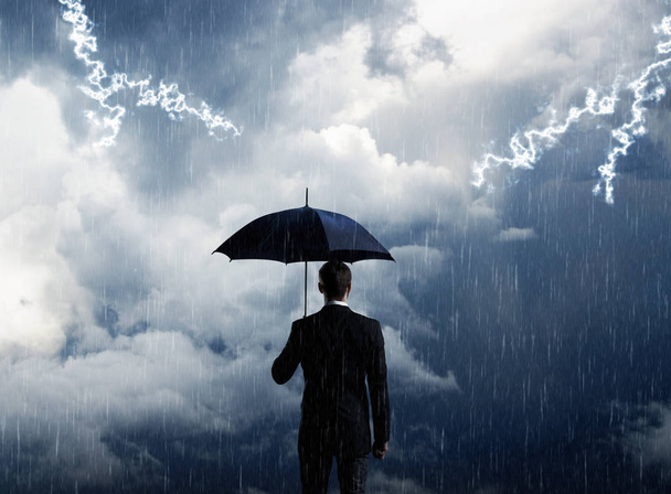 Businessman with umbrella standing over stormy background. - Zdjęcie, obraz