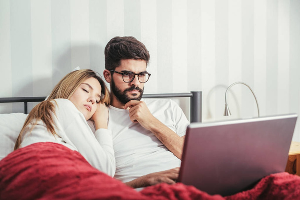 Young couple with laptop in the bed in room - Foto, imagen
